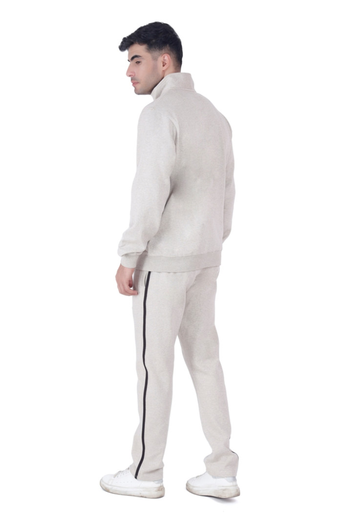 A man in a Turfit’s Oatmeal Millage tracksuit with black side piping, shown from the back while slightly turning his head, wearing white sneakers and standing against a plain white background.